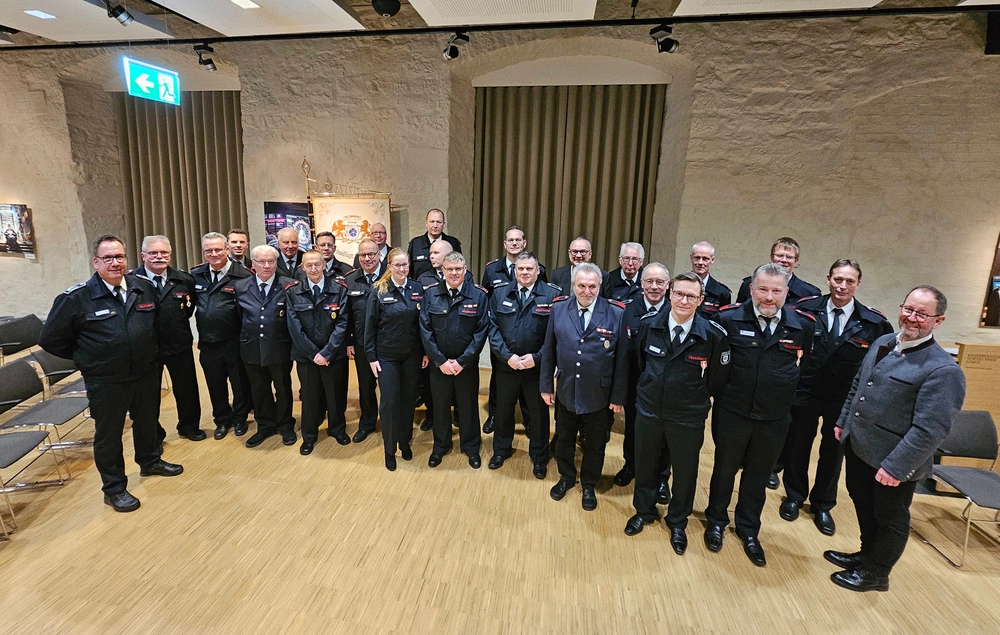Zwei Dutzend Feuerwehrleute halten Urkunden und Blumensträuße in den Händen.