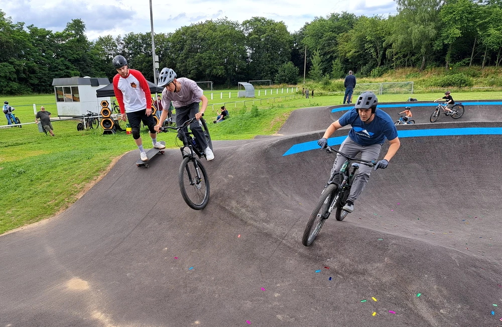 Man sieht Skateboard- und Radfahrer auf dem Pumptrack
