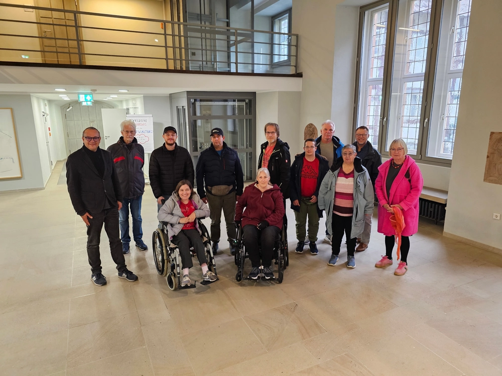 Mehrere Menschen, teilweise im Rollstuhl, stehen bzw. sitzen in der Halle des Rathauses