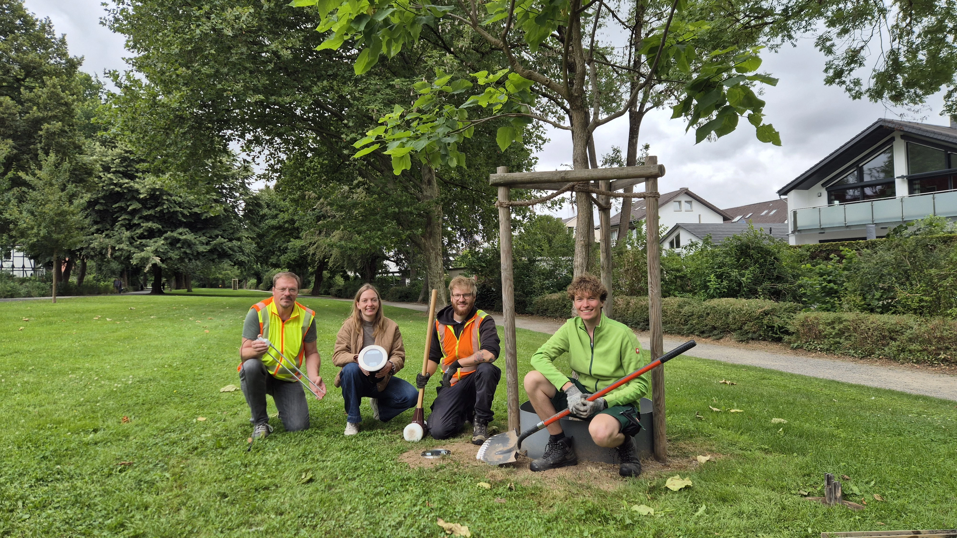 Vier Menschen knien mit Technik in der Hand neben einem jungen Baum.