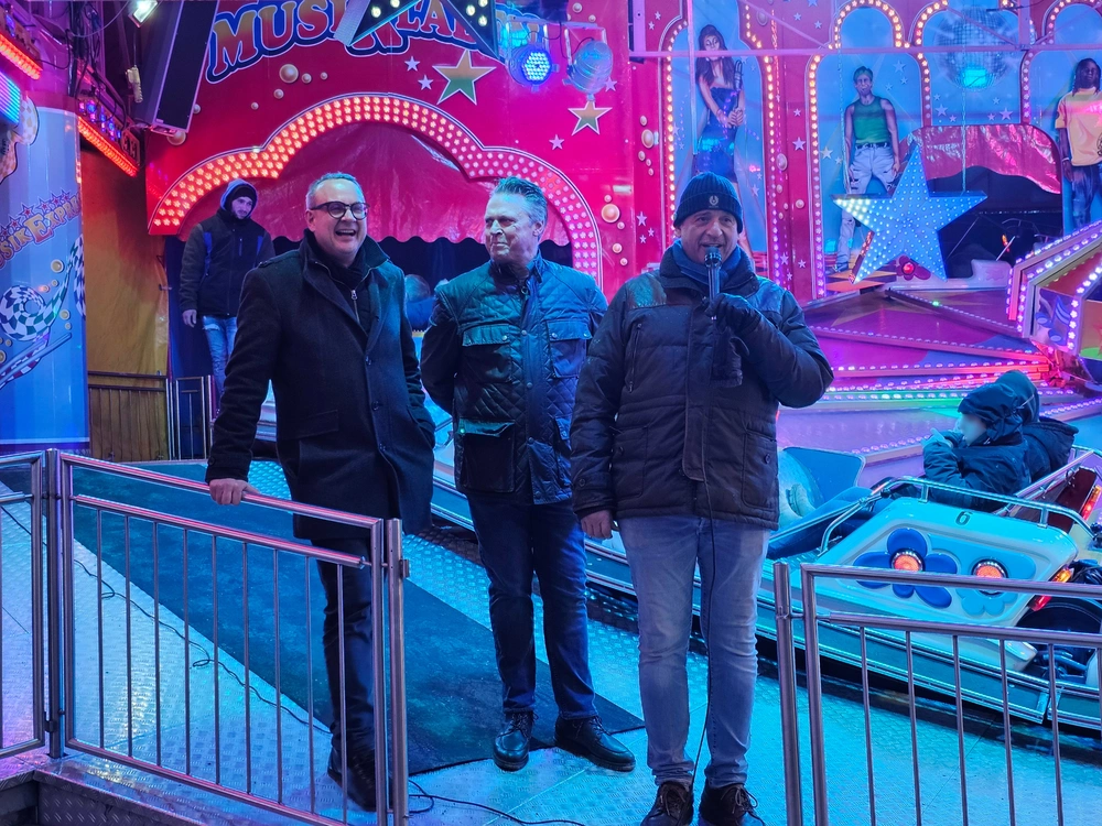 Drei Männer stehen vor einem Kirmes-Fahrgeschäft.