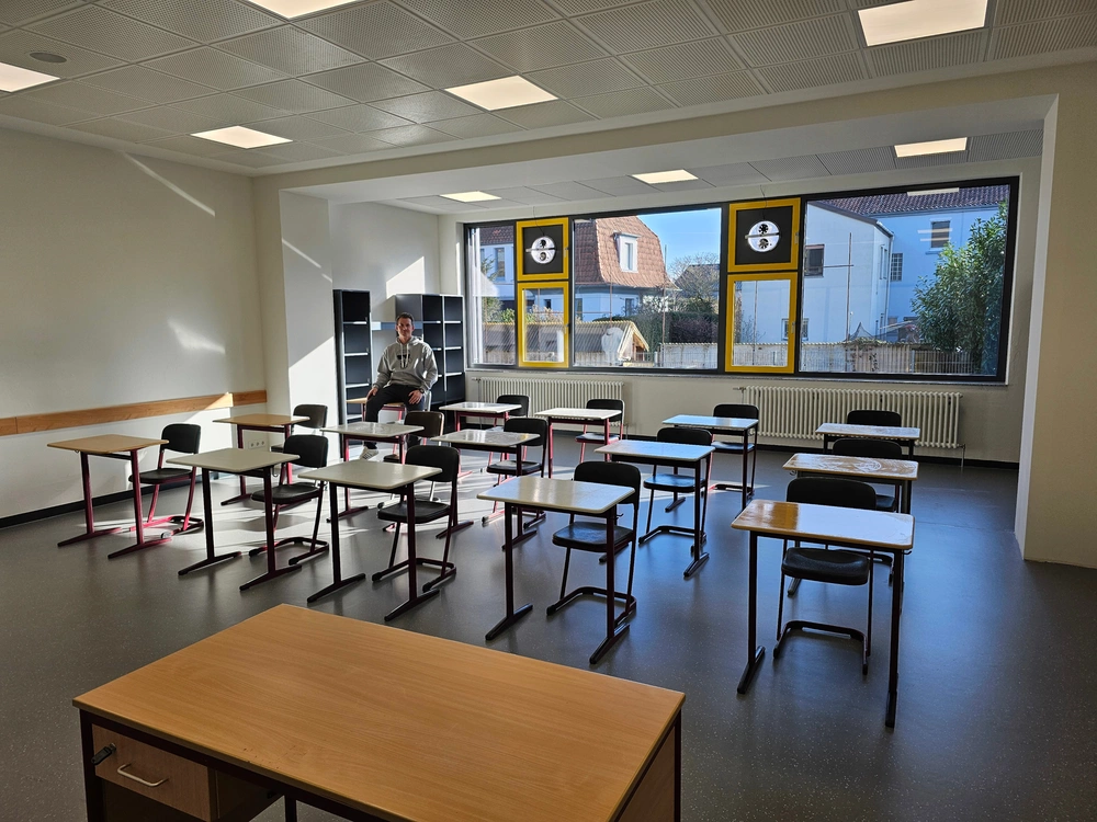 Ein Mann sitzt auf einem Tisch in einem Klassenzimmer.