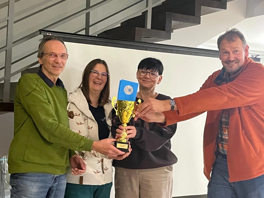 Vier Personen halten gemeinsam einen goldenen Pokal in den Händen.