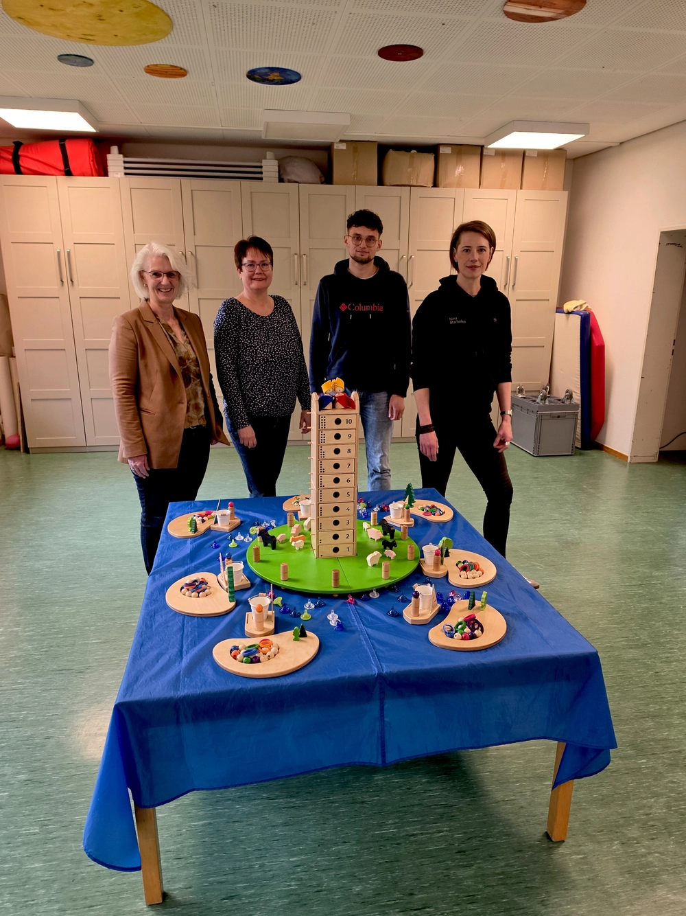 Vier Menschen stehen hinter einem kleinen Tisch mit bunten Holzklötzen und Spielfiguren.
