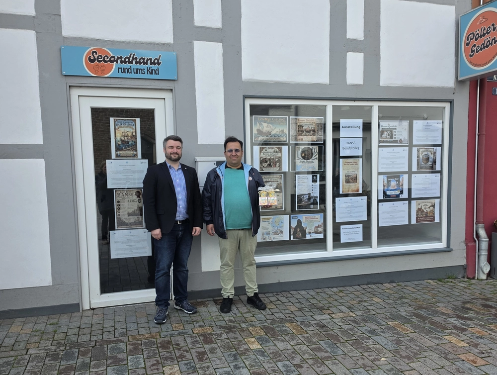 Zwei Männer stehen vor einem Schaufenster, in das Plakate geklebt sind.
