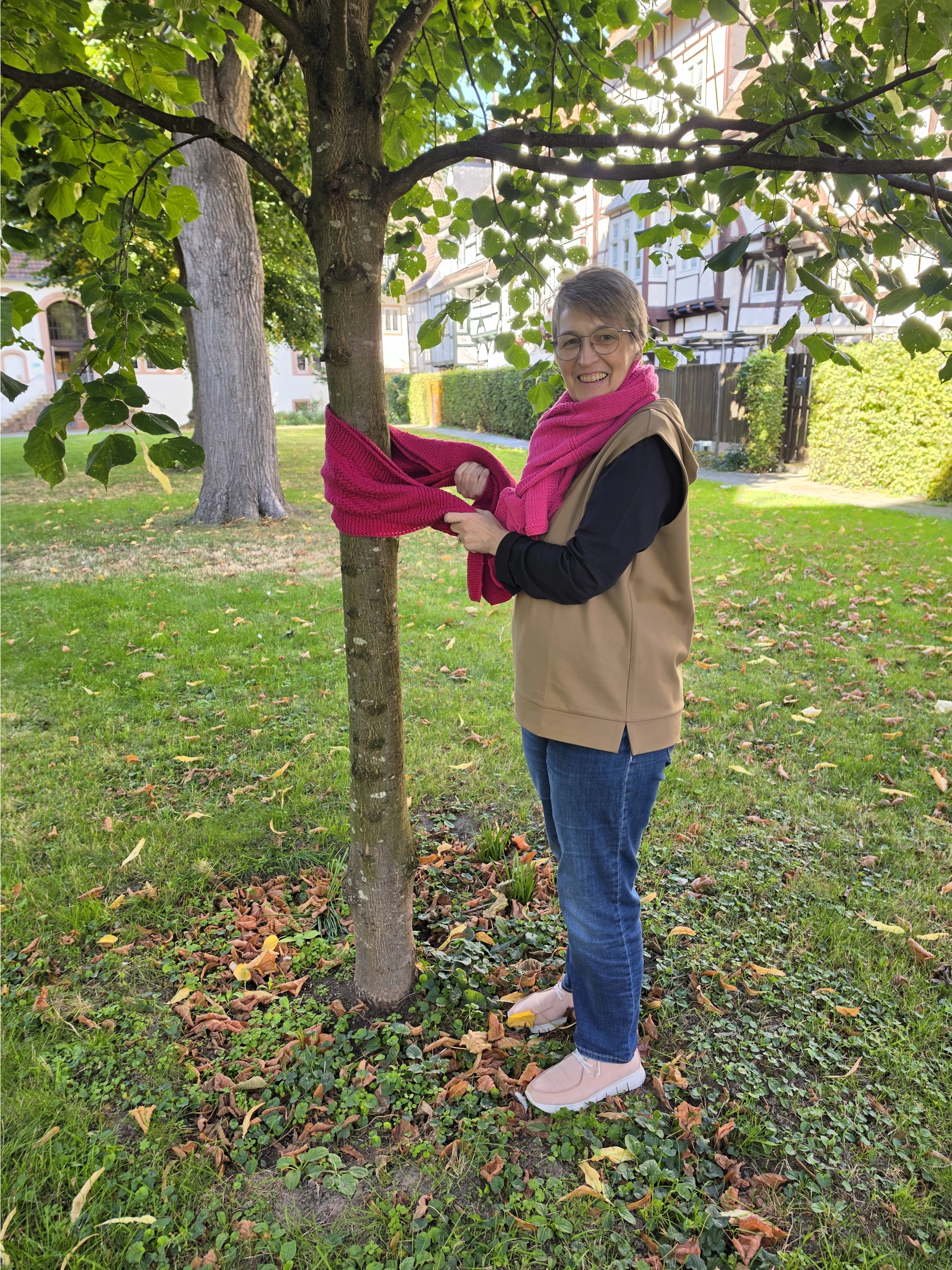Eine Frau, die einen pinken Schal um den Hals trägt, bindet einen pinken Schal um einen Baum.
