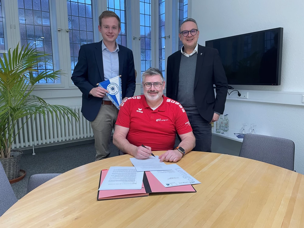 Der Vorsitzende des Stadtsportverbandes, Alexander Wegner, unterzeichnet den neuen Pakt für den Sport. Janik Wiemann (links) und Bürgermeister Markus Baier (rechts) schauen ihm dabei über die Schulter.