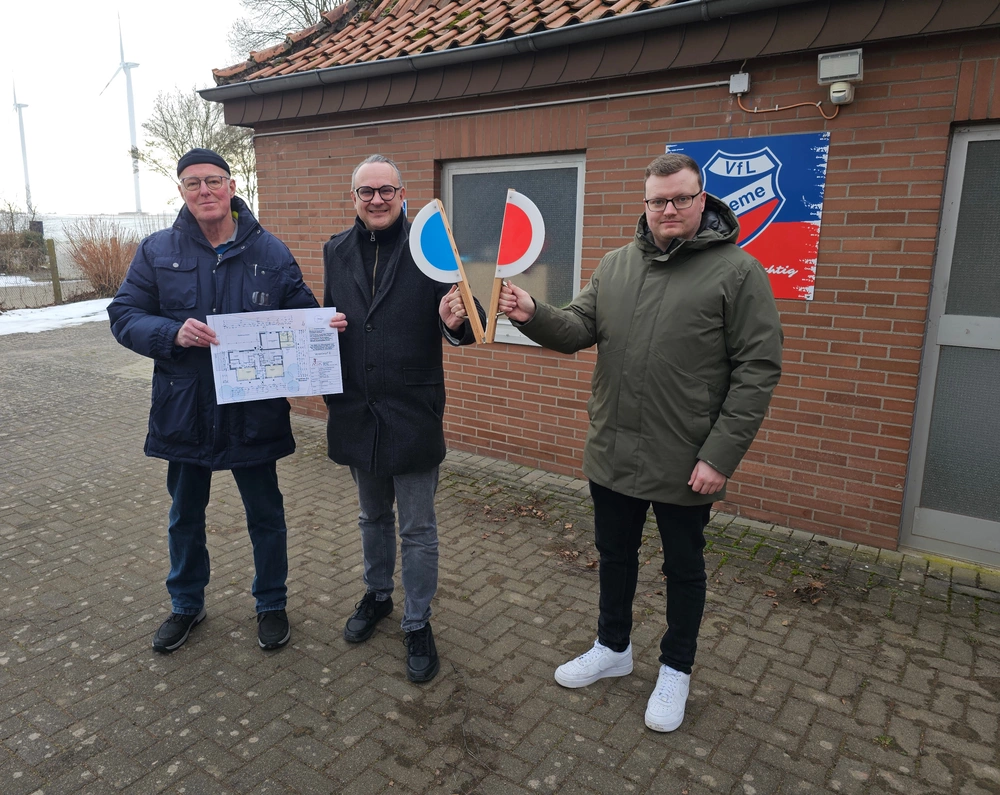 Drei Männer stehen nebeneinander, einer hält eine Bauzeichnung, die anderen beiden halten eine Startklappe.
