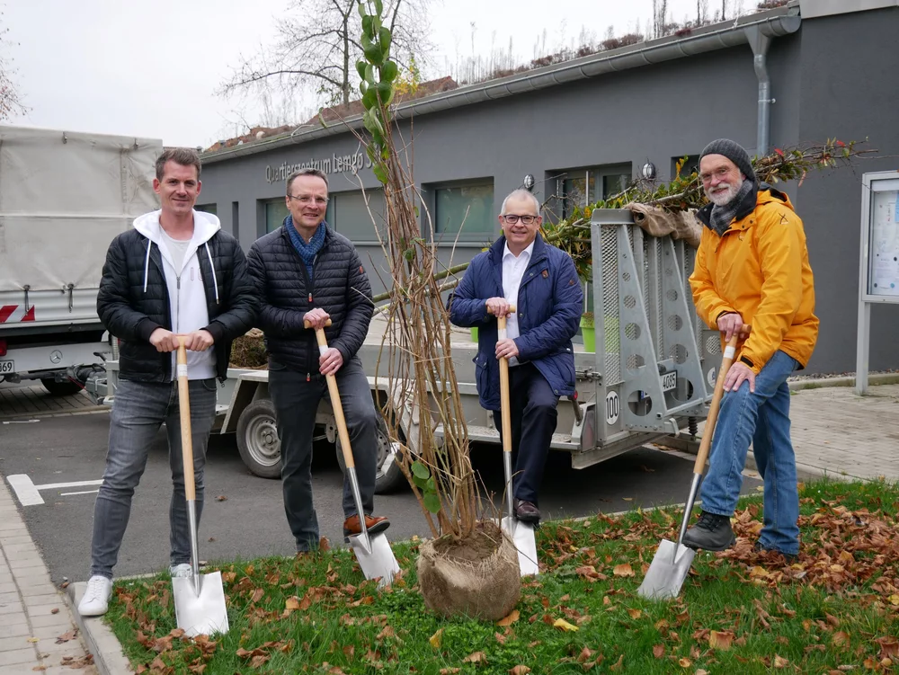 Norman Rackisch (Gebäudewirtschaft Lemgo), Roman Paschek (CDU Lemgo), Michael Seidel (Fielmann Group) und Karl-Heinz Mense (Nachbarschaft Lemgo Süd) mit Spaten und einem Baum vor der Mehrzweckhalle Laubke.