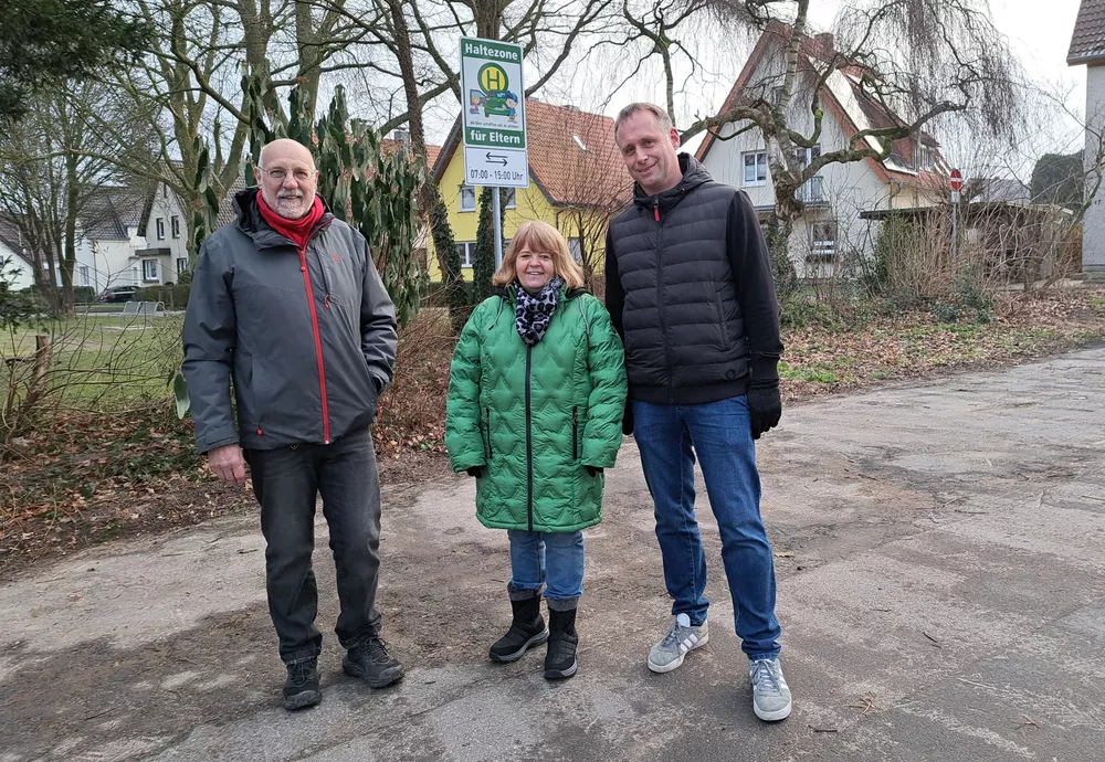 Elternhaltestelle in Brake: Hartmut Baack (Ortsausschussvorsitzender Brake), Gerlinde Schidt (Leiterin des Familienzentrums Brake) und Jörg Franks (Leiter der Grundschule am Schloss, von links) vor dem Schild, das an der Ewerbeckstraße auf die Elternhaltestelle hinweist.