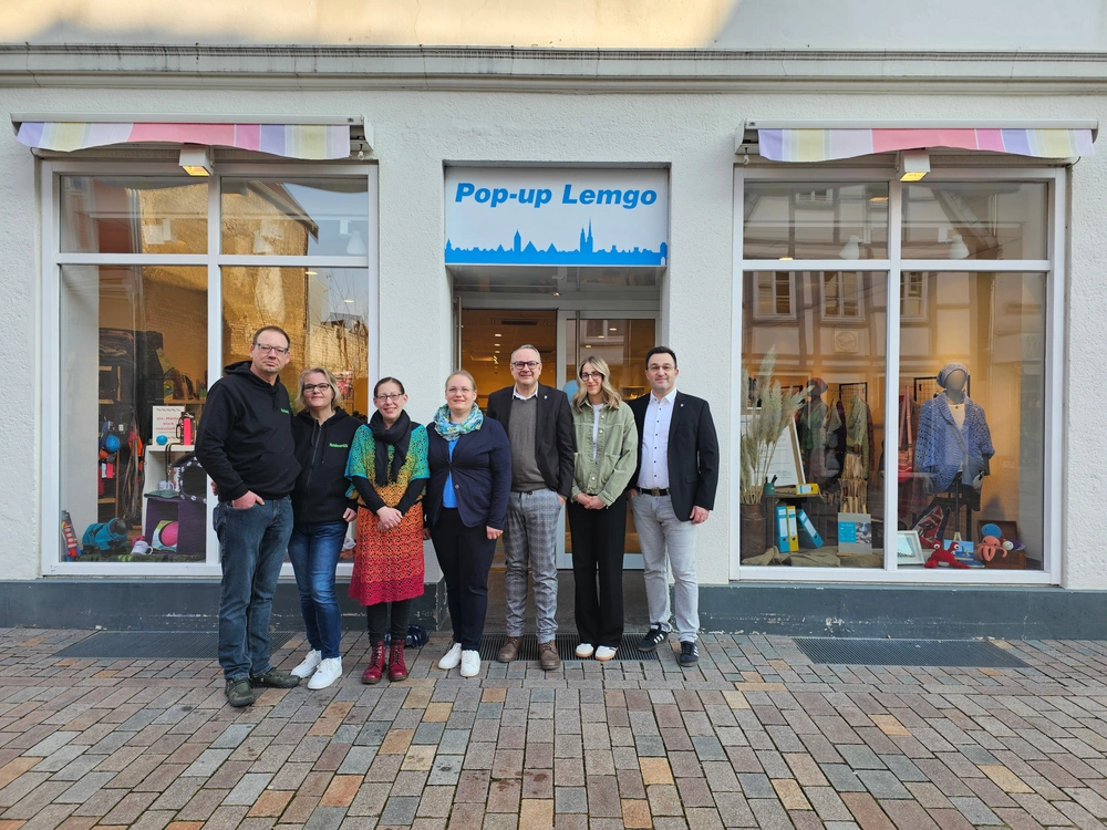 Eine Gruppe von Menschen steht vor einem Ladengeschäft, über dem ein Schild "Pop-up Lemgo" hängt.