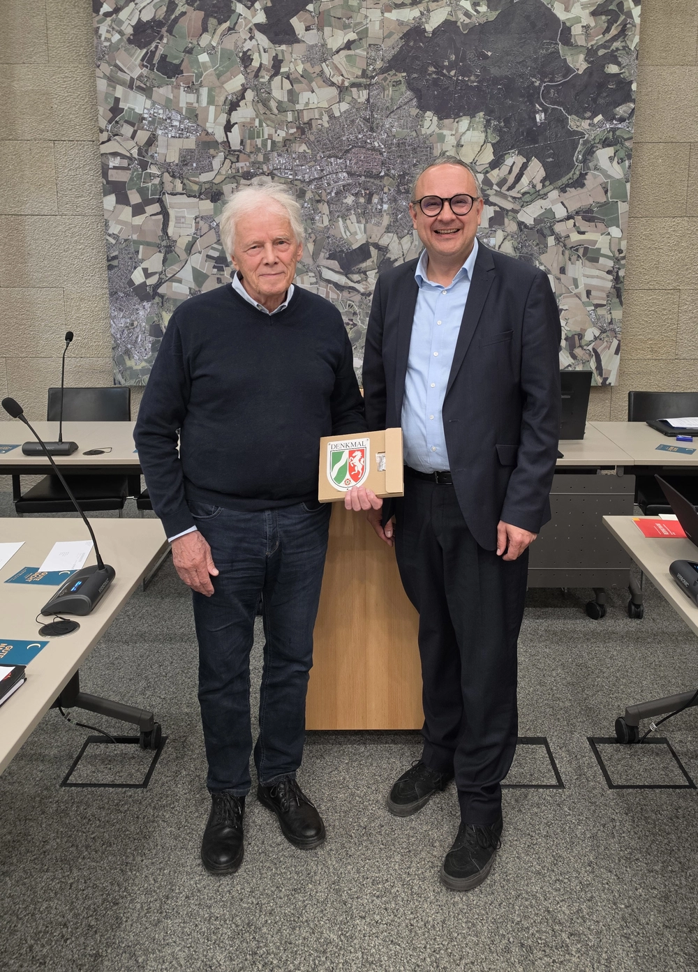 Zwei Männer stehen nebeneinander. Der Ältere hält eine Denkmal-Plakette in den Händen.