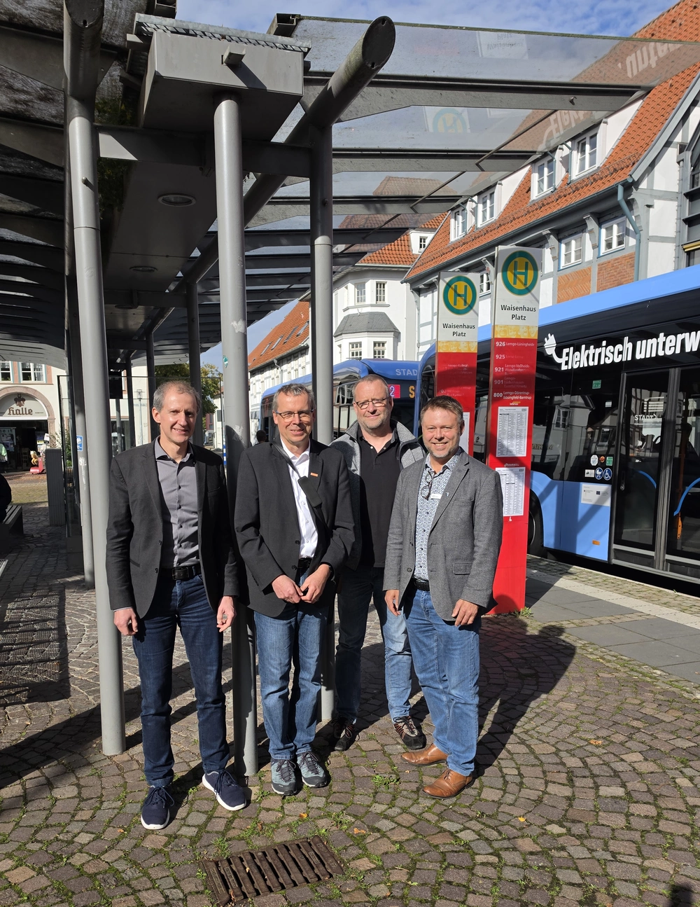 Mehrere Menschen stehen an einer Bushaltestelle. Im Hintergrund ist ein Lemgoer Stadtbus zu sehen.