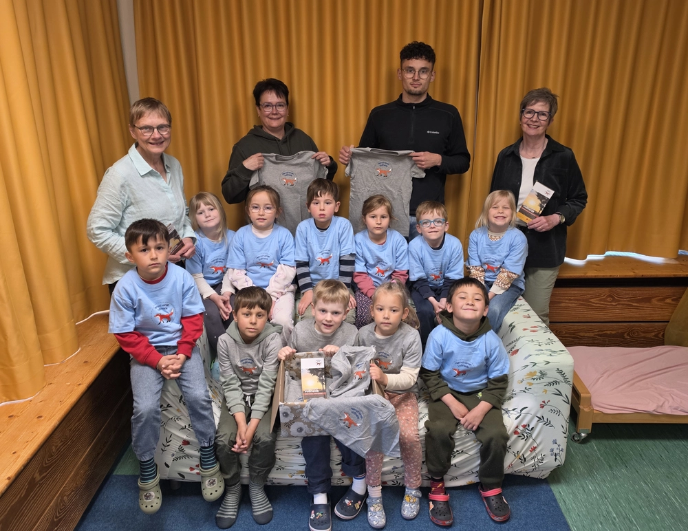 Eine Gruppe von Kindergartenkindern und ein paar Erwachsene sind zu sehen. Die Kinder haben gleiche T-Shirts an.