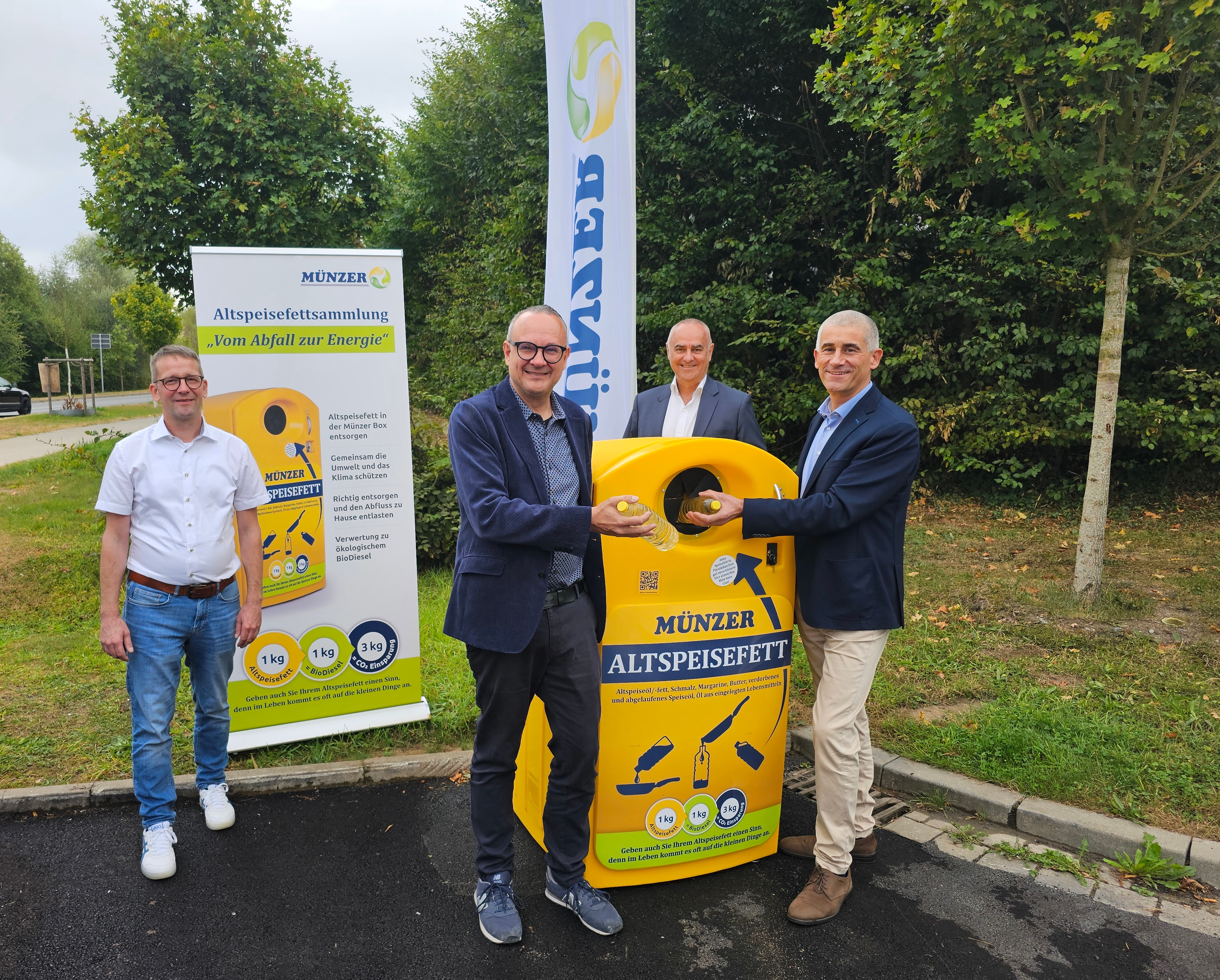 Vier Männer stehen um eine gelbe Sammelbox, in die zwei von ihnen Plastikflaschen mit Öl einwerfen.