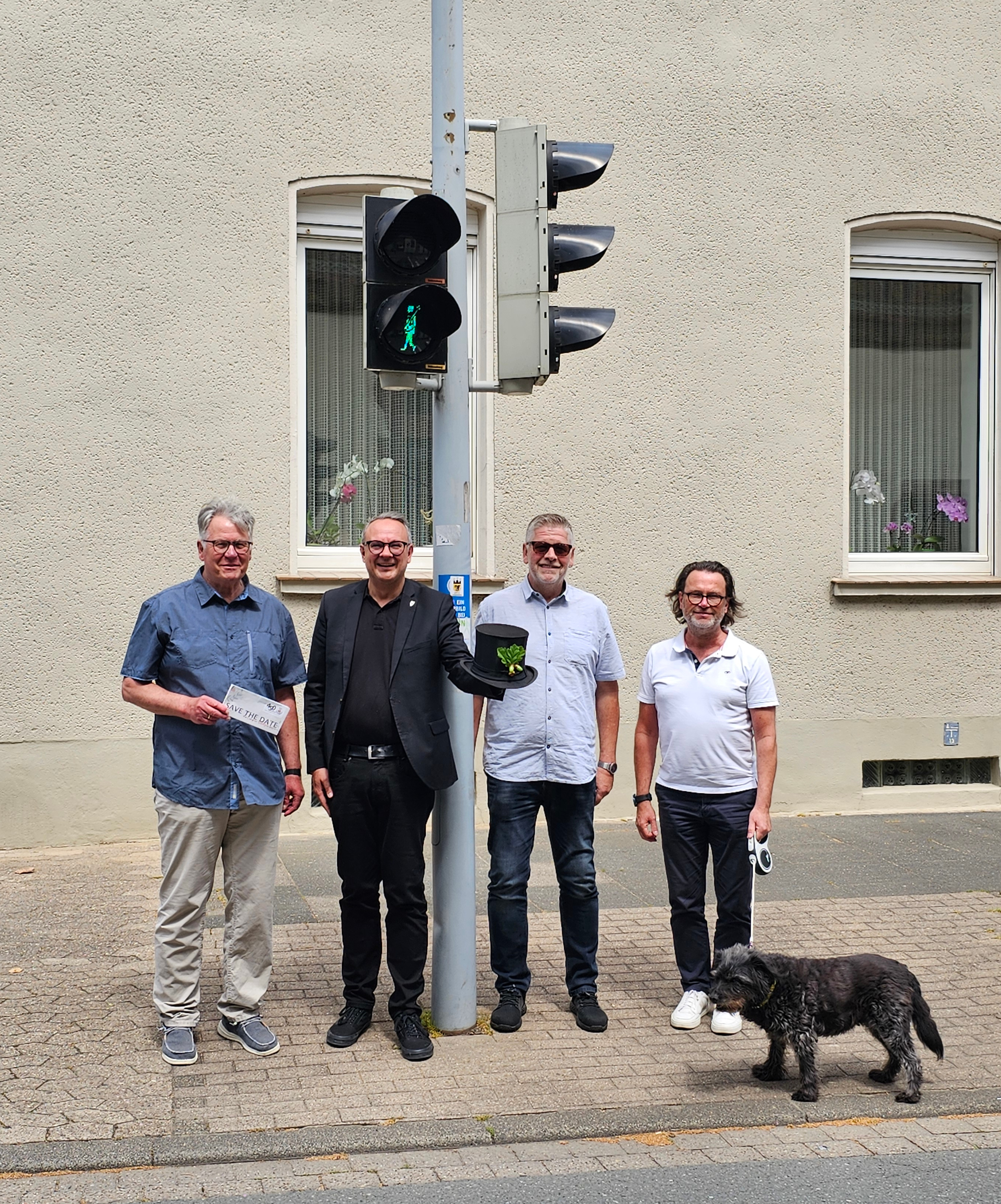 Vier Männer stehen vor einer Ampel, an der ein grünes Ampelmännchen in Form eines Schützen leuchtet.
