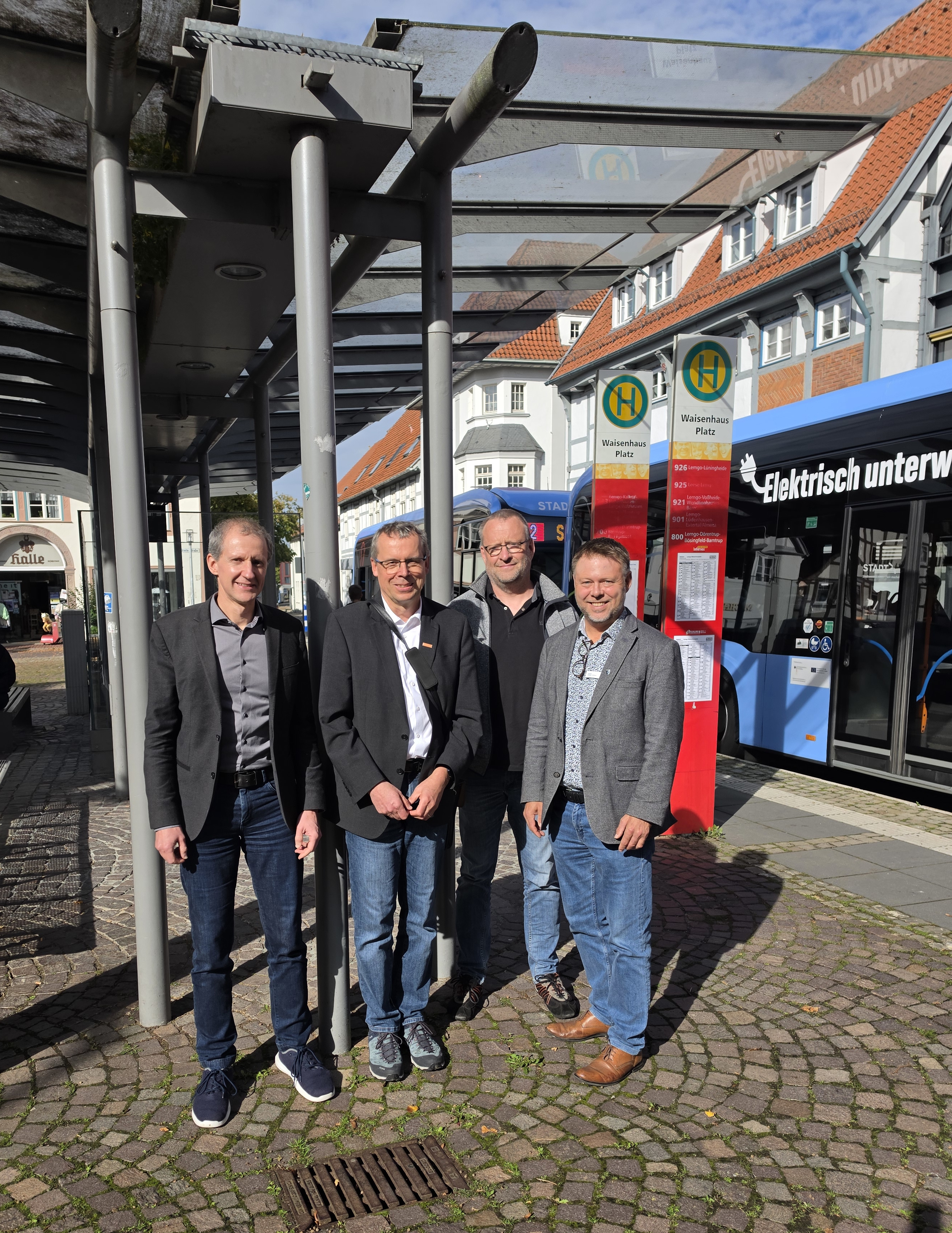 Mehrere Menschen stehen an einer Bushaltestelle. Im Hintergrund ist ein Lemgoer Stadtbus zu sehen.