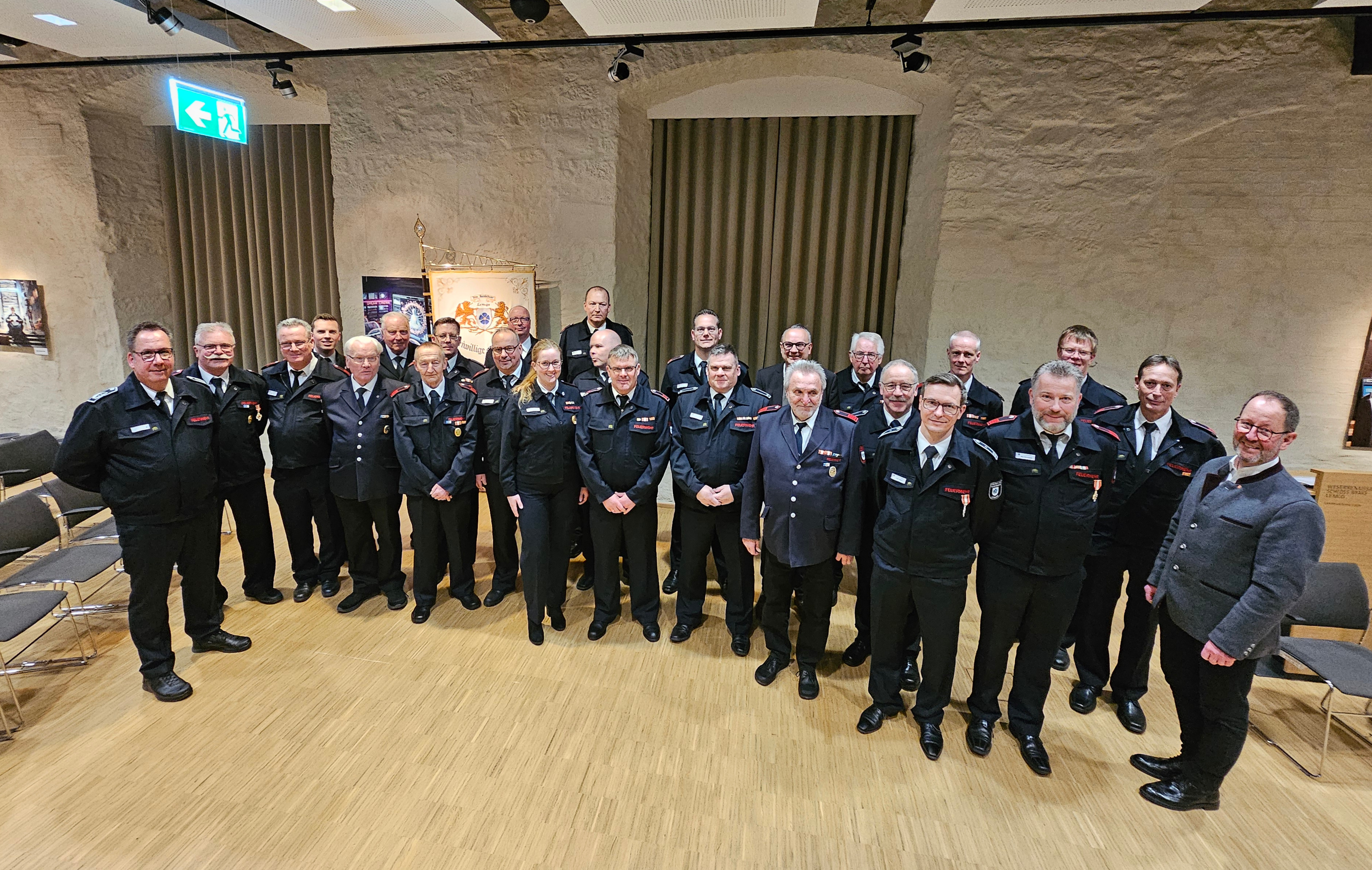 Zwei Dutzend Feuerwehrleute halten Urkunden und Blumensträuße in den Händen.