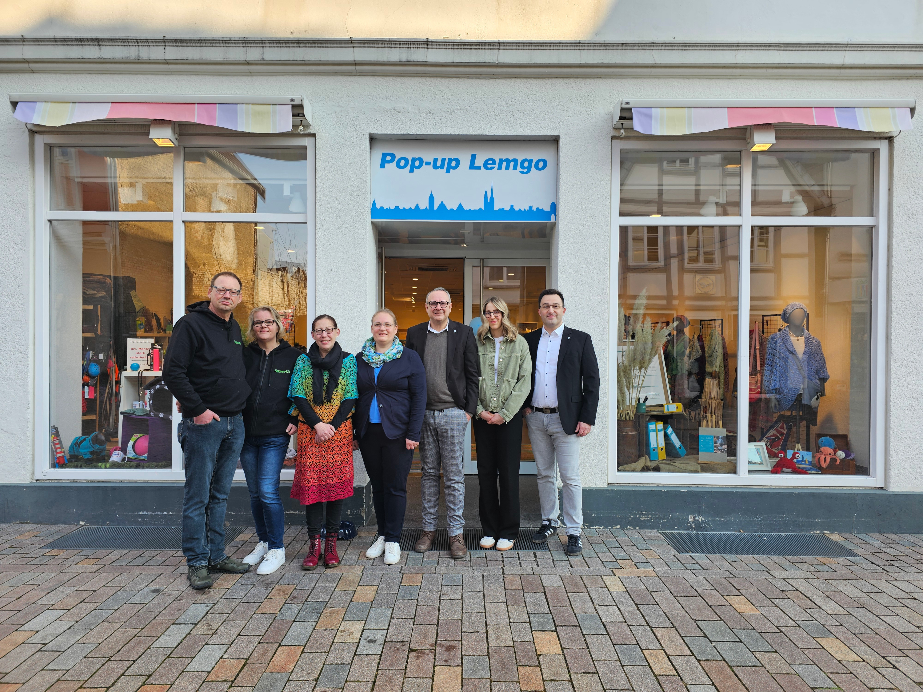 Eine Gruppe von Menschen steht vor einem Ladengeschäft, über dem ein Schild "Pop-up Lemgo" hängt.