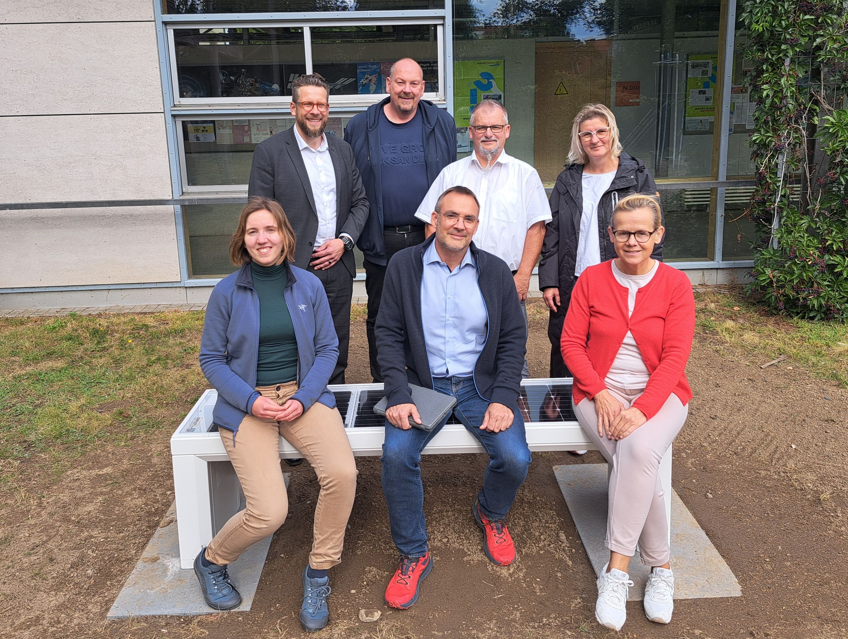 Mehrere Menschen sitzen auf und stehen hinter einer Bank mit Solarmodulen in der Sitzfläche.