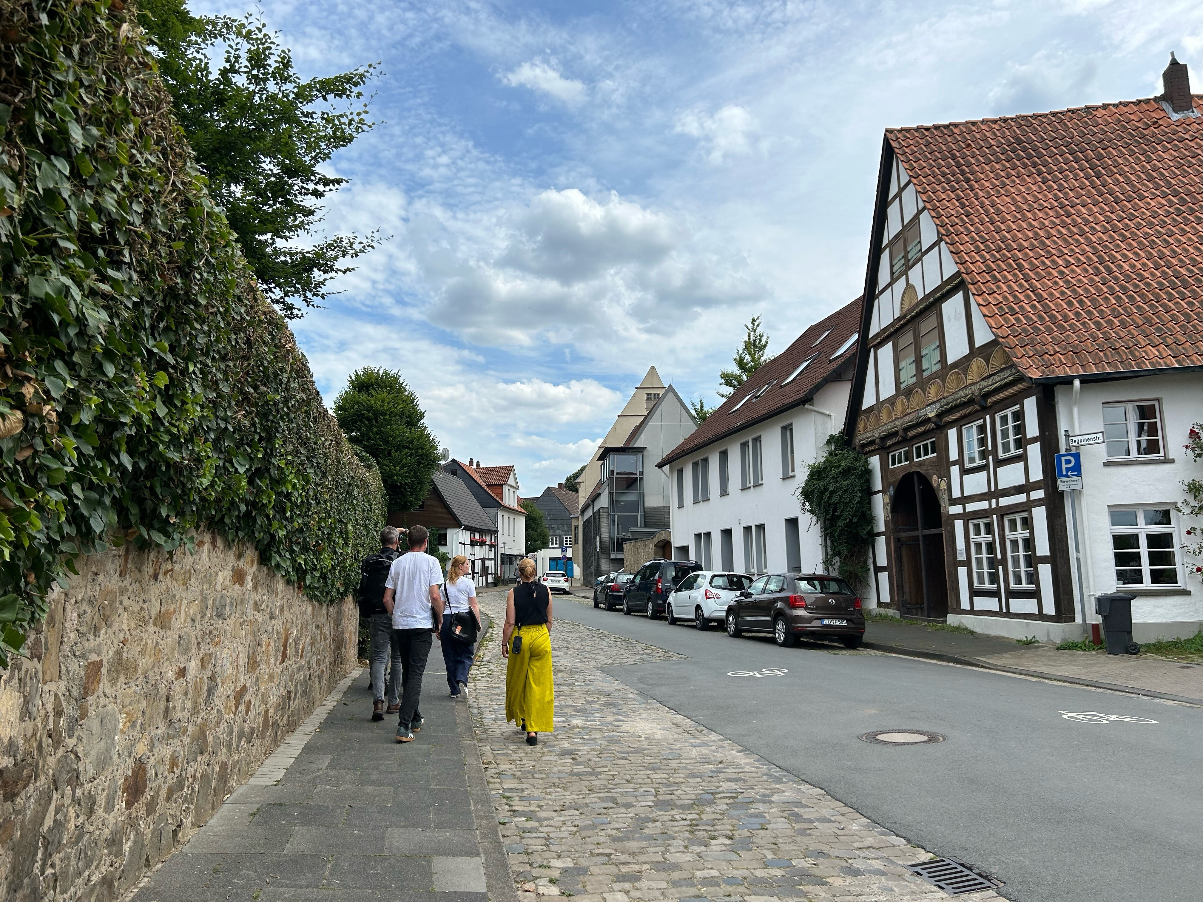 Menschen gehen auf dem Bürgersteig an einer historischen Mauer und Fachwerkhäusern entlang